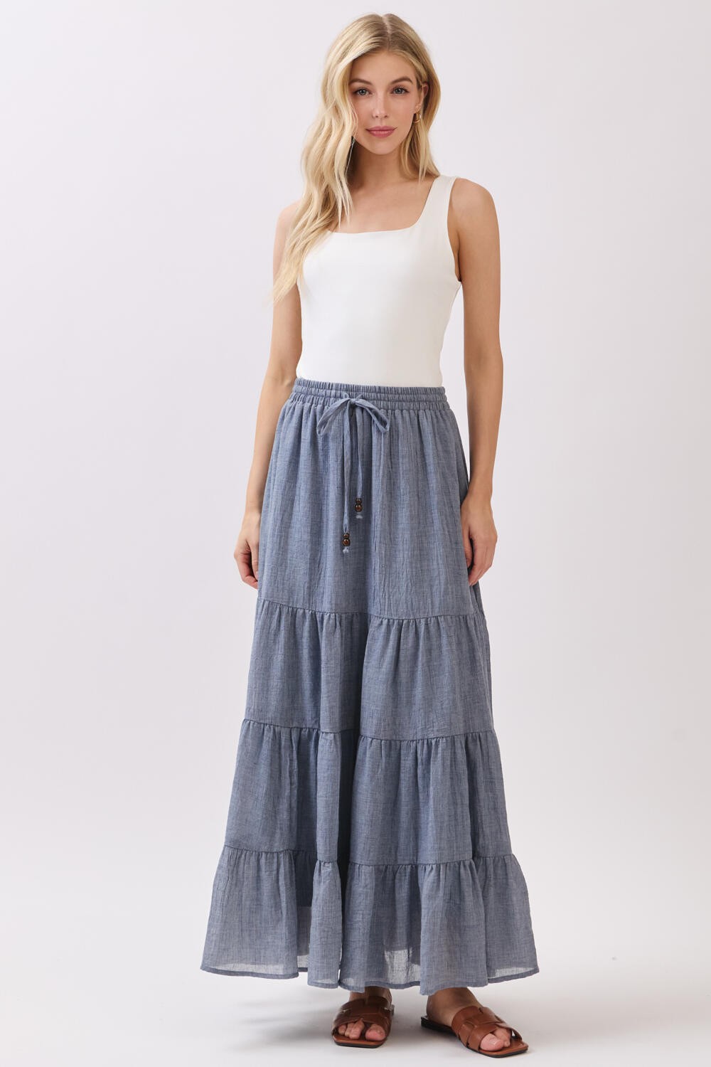 woman wearing a white tank top and a long tiered blue maxi skirt with an elastic waistband and drawstring