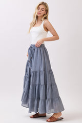 woman wearing a fitted white tank top and a long blue tiered maxi skirt with an elastic waist and drawstring