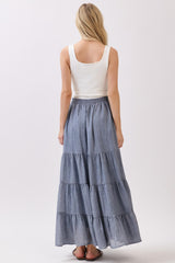 woman wearing a white sleeveless top and a chambray tiered maxi skirt, viewed from the back