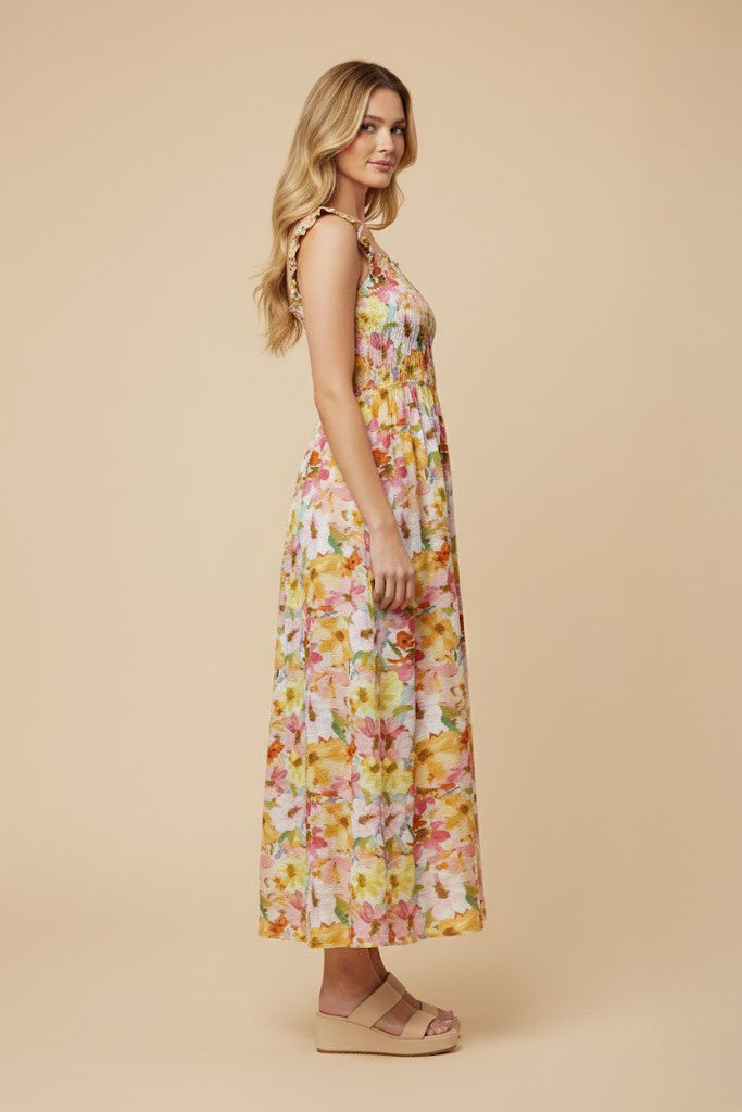 woman wearing a floral maxi dress in yellow, pink, and orange with adjustable straps and a tiered skirt
