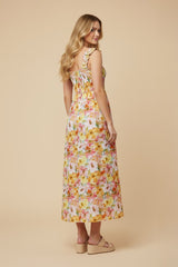 woman wearing a floral maxi dress with smocked back and ruffled straps, standing turned slightly away from the camera