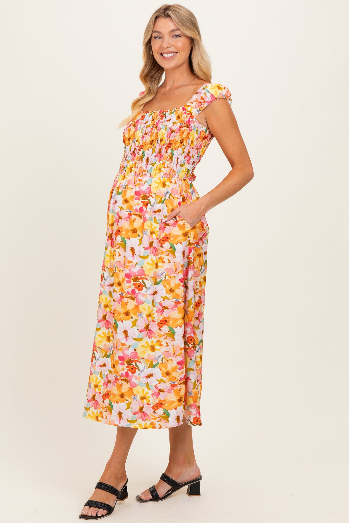 woman wearing a floral maternity dress with a smocked bodice and pockets, showcasing her baby bump