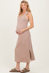 woman wearing a beige ribbed maternity maxi dress with side slits and holding her baby bump