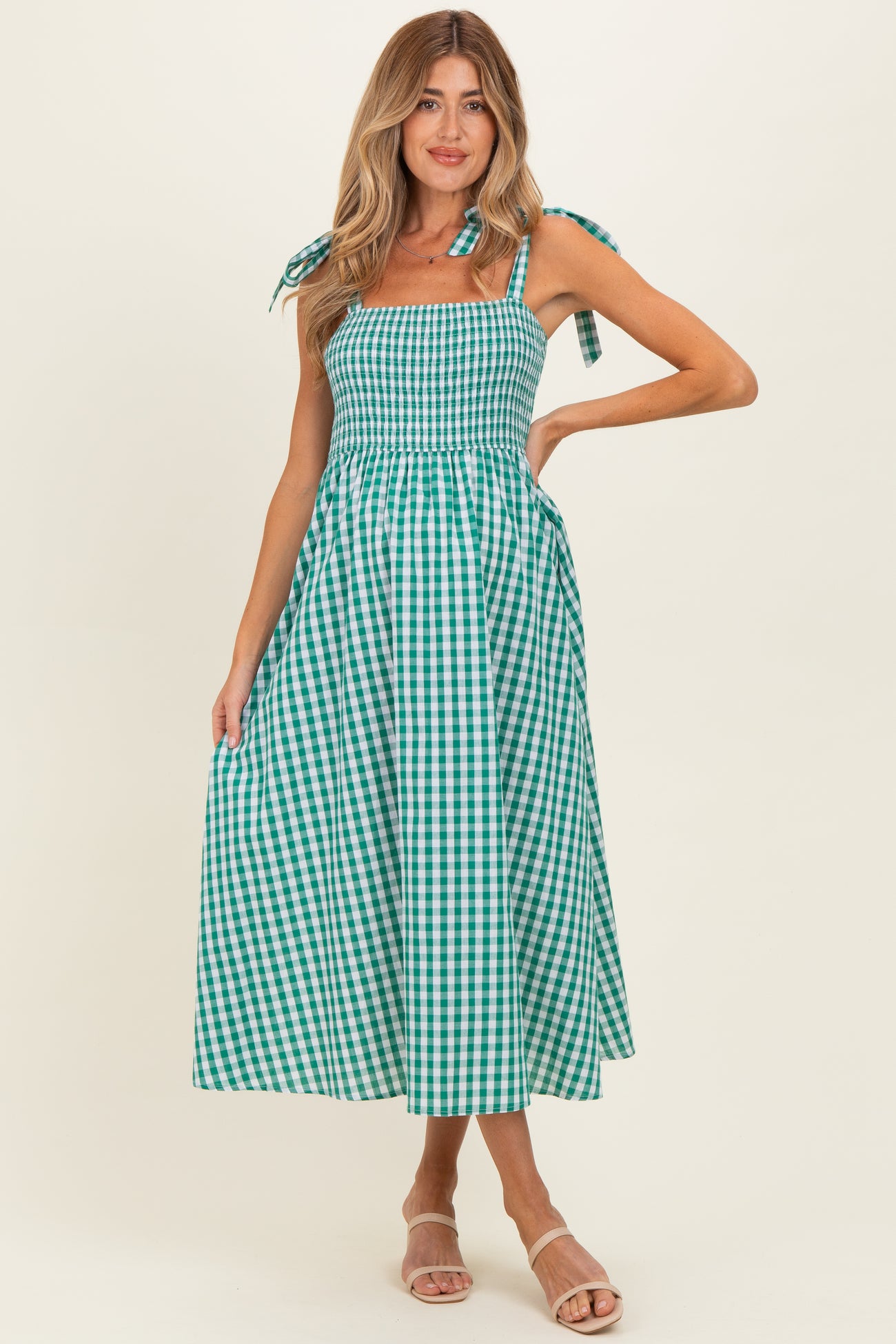 woman wearing a green and white gingham maternity maxi dress with tie shoulder straps and a smocked bodice, showing a baby bump