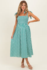 woman wearing a green and white gingham maternity maxi dress with tie shoulder straps and a smocked bodice, showing a baby bump