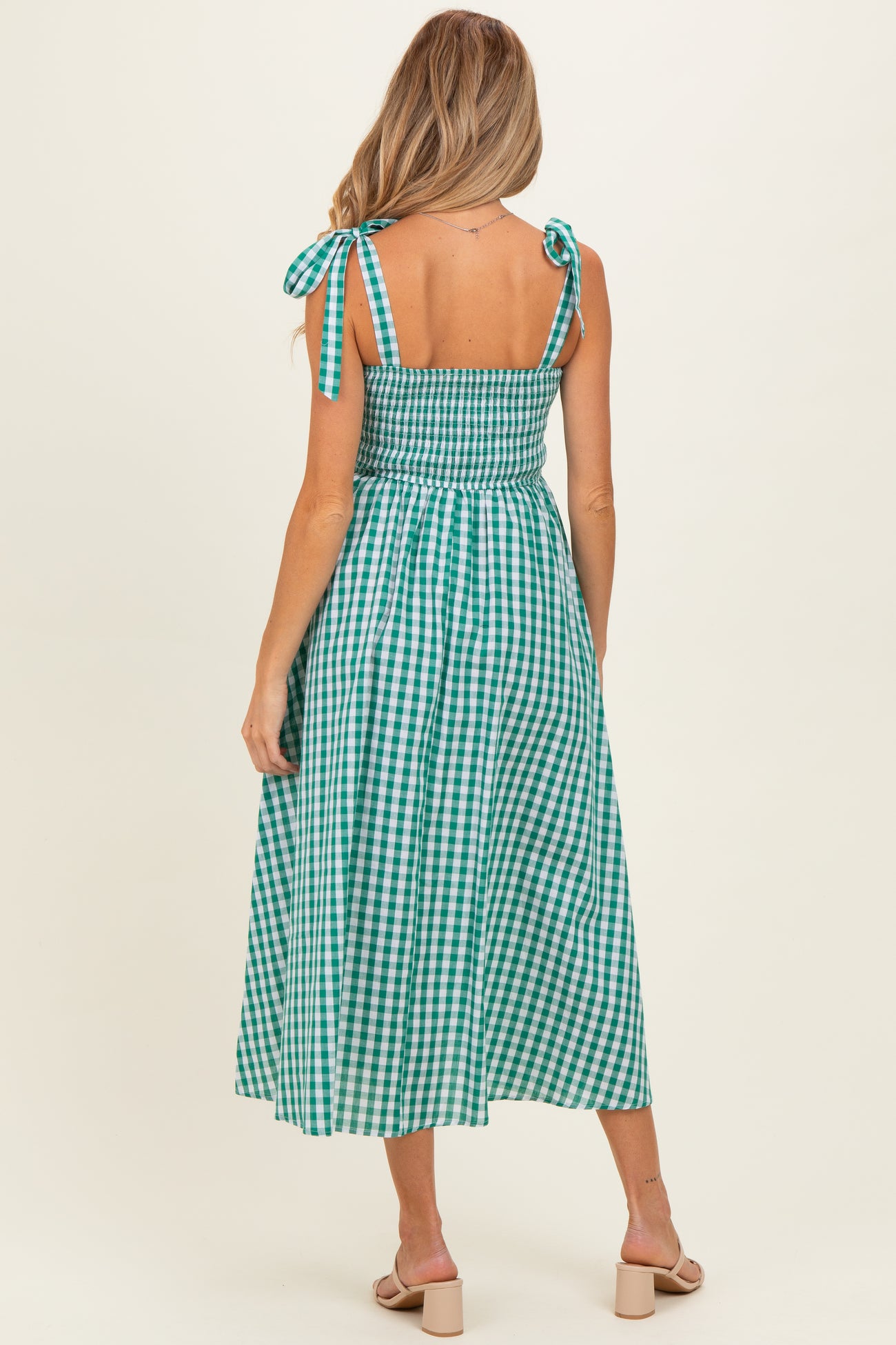 woman wearing a green and white gingham maternity dress with tie shoulder straps and a smocked back