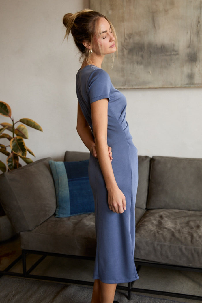 woman wearing a fitted slate blue midi dress, standing sideways with her hand on her hip