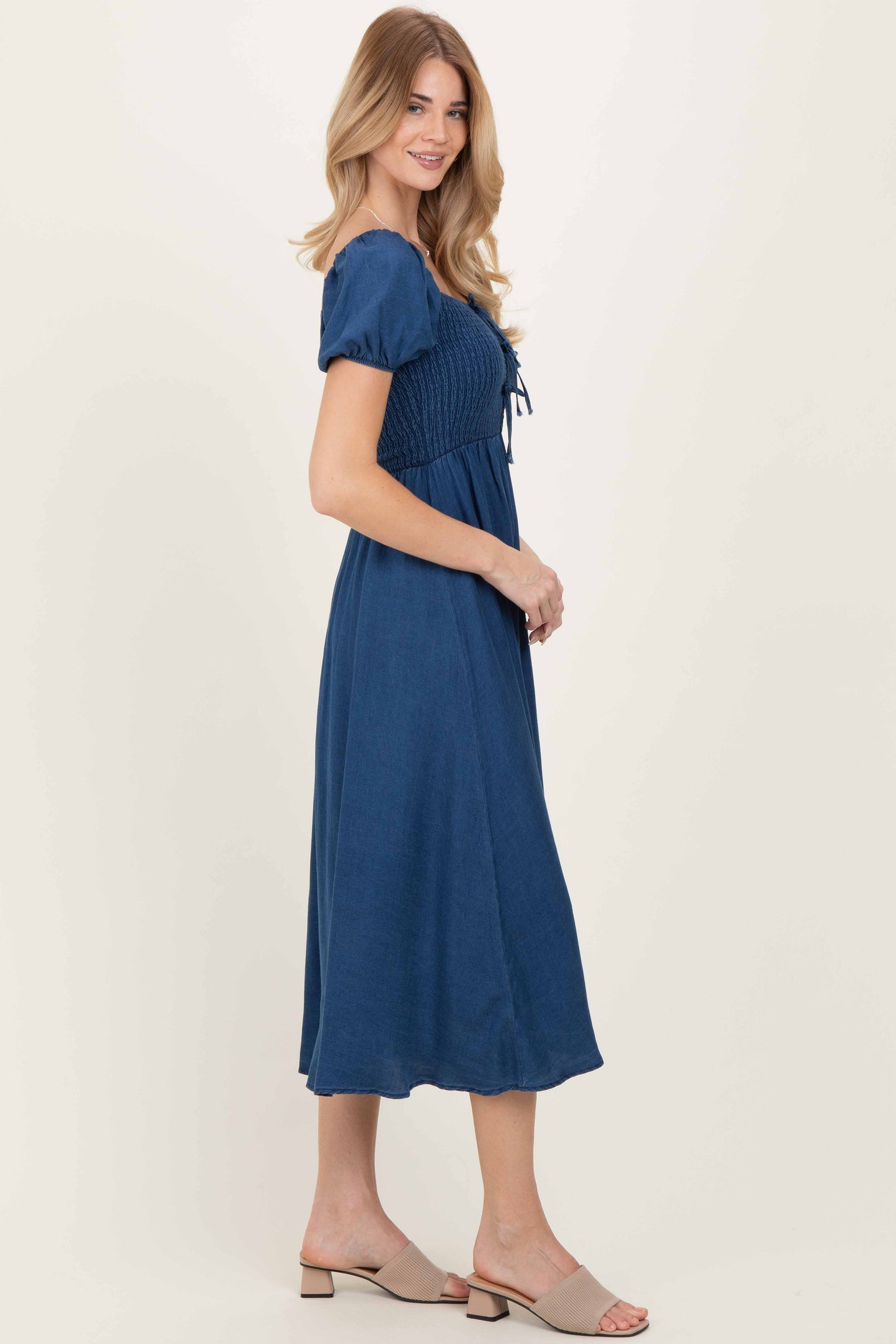 woman wearing a navy blue smocked midi dress with puff sleeves and tied front detail