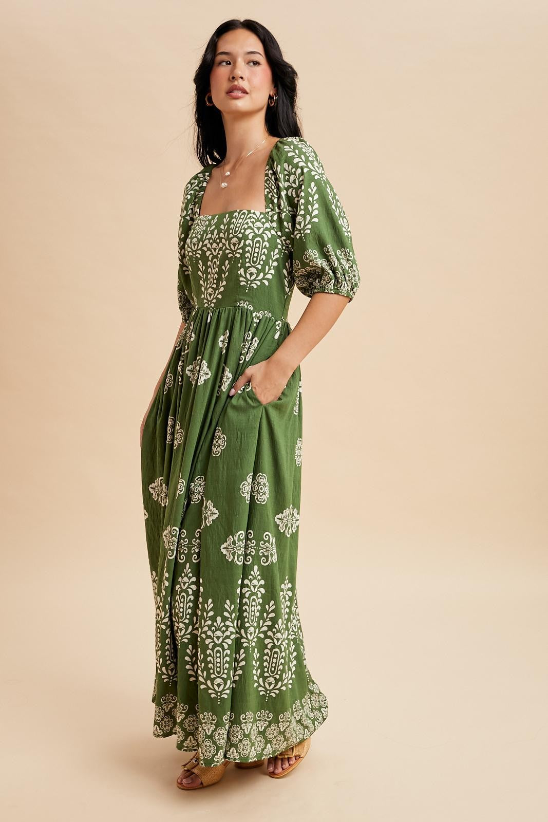 woman wearing a green maxi dress with white floral patterns and puff sleeves, standing with hands in pockets