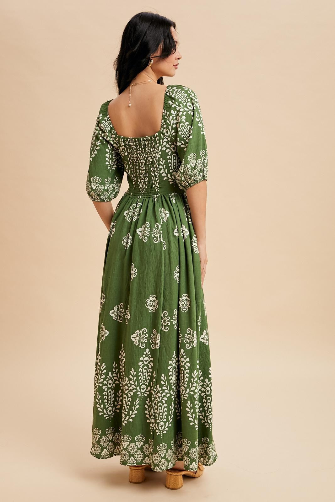 woman wearing a green maxi dress with puff sleeves and white floral patterns, showing the back view