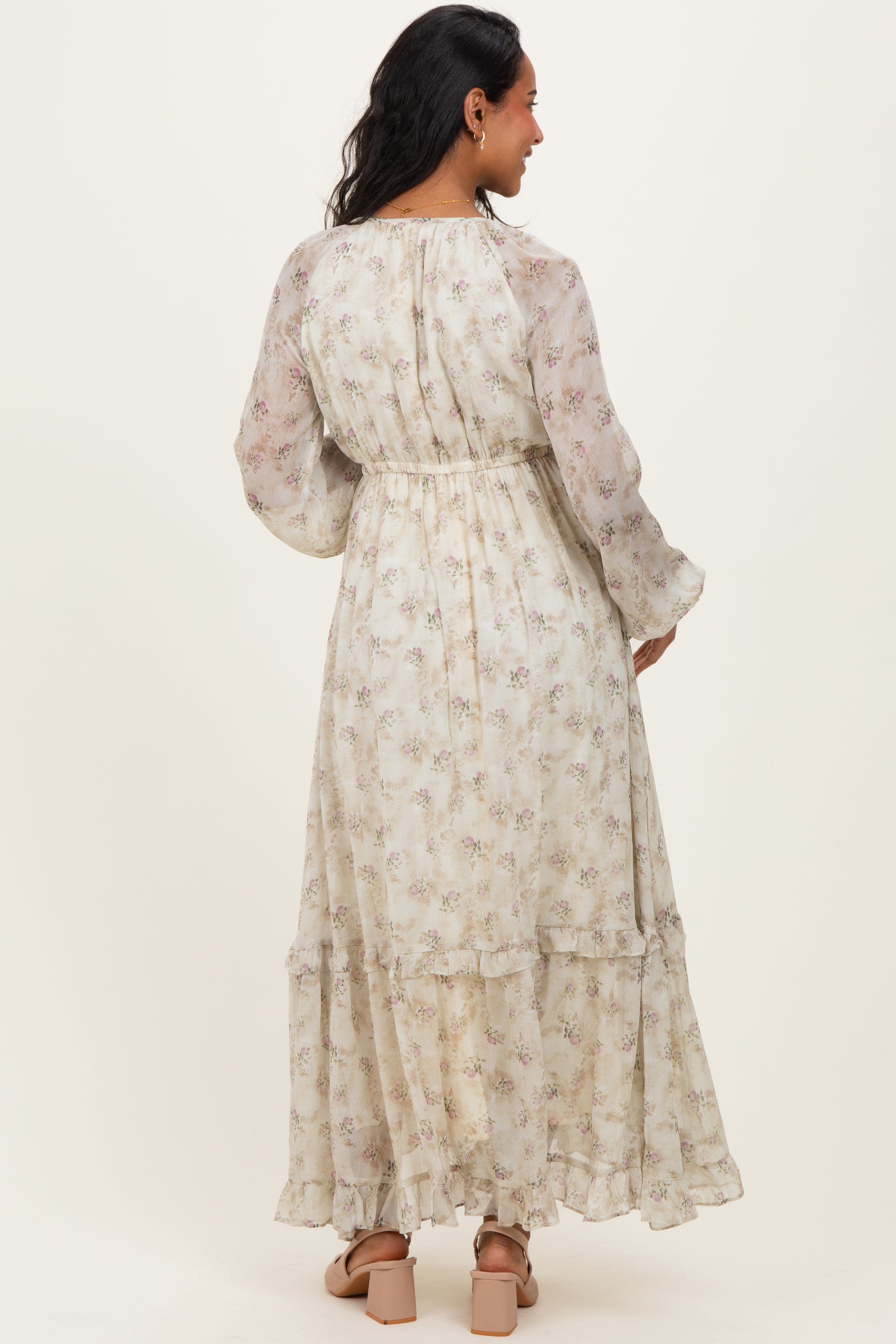 woman wearing a floral patterned long sleeve maternity dress with a tiered skirt and elastic waist, showing a baby bump