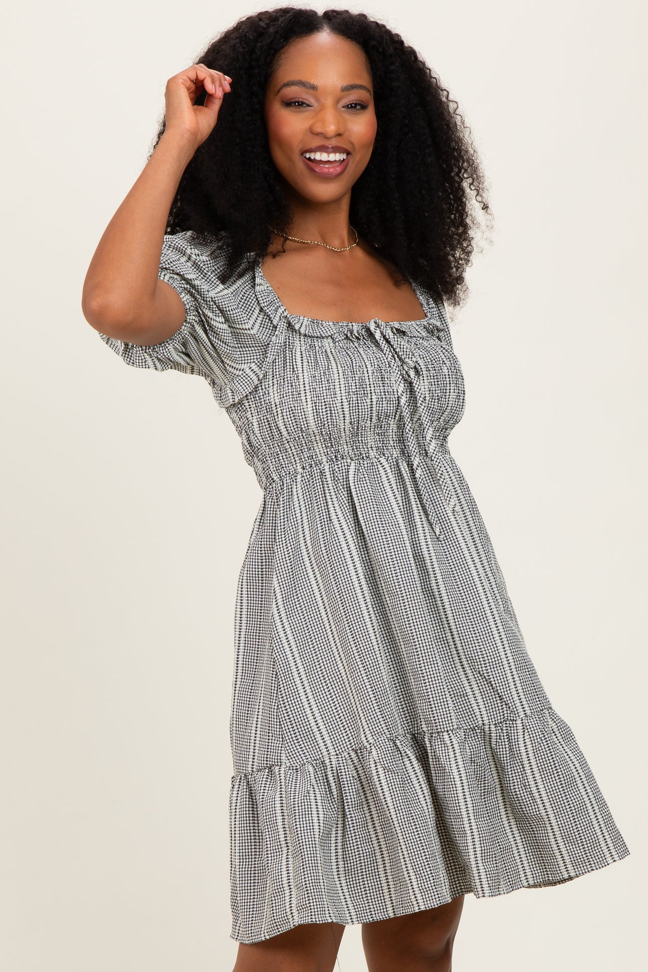woman wearing a black and white checkered short puff sleeve dress with a square neckline and ruffled hem