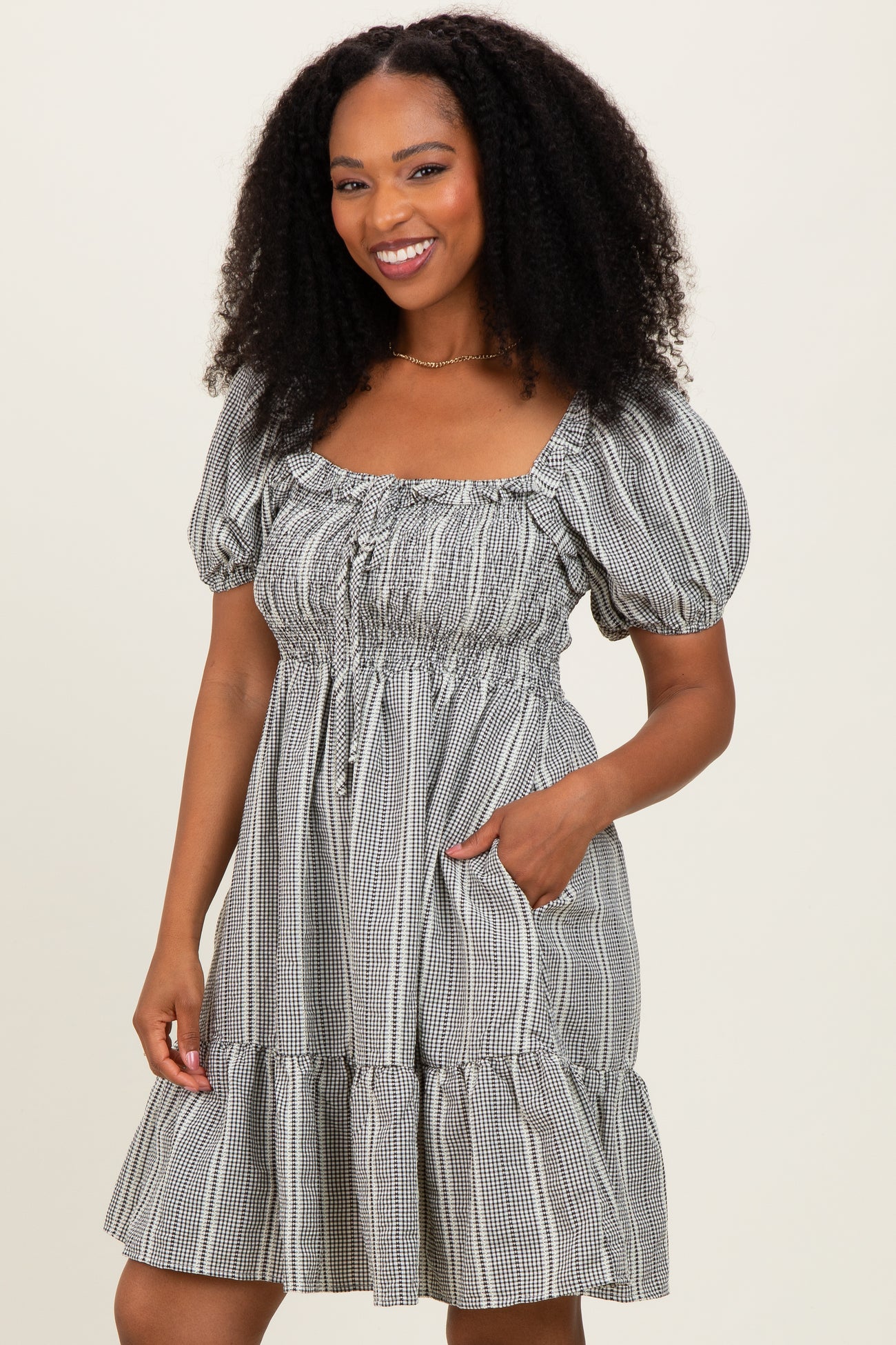 woman wearing a black and white checkered puff sleeve mini dress with a square neckline and pockets