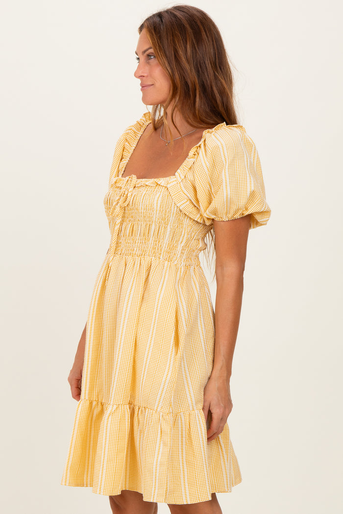 woman wearing a yellow gingham puff sleeve mini dress with smocked bodice and ruffled hem