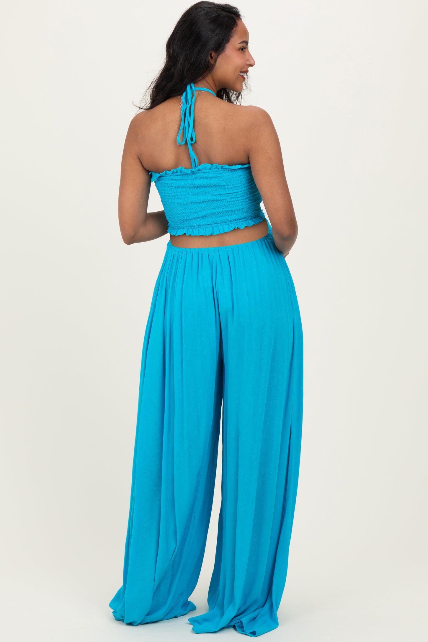woman wearing a bright blue maternity crop top and wide-leg pants, showing a baby bump from the back