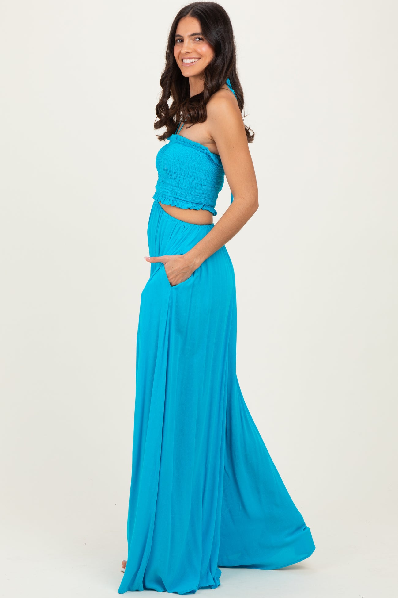 woman wearing a bright blue halter neck maxi dress with a smocked bodice and pockets, standing sideways