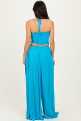 woman wearing a blue two-piece outfit with a smocked crop top and flowy wide-leg pants, view from the back