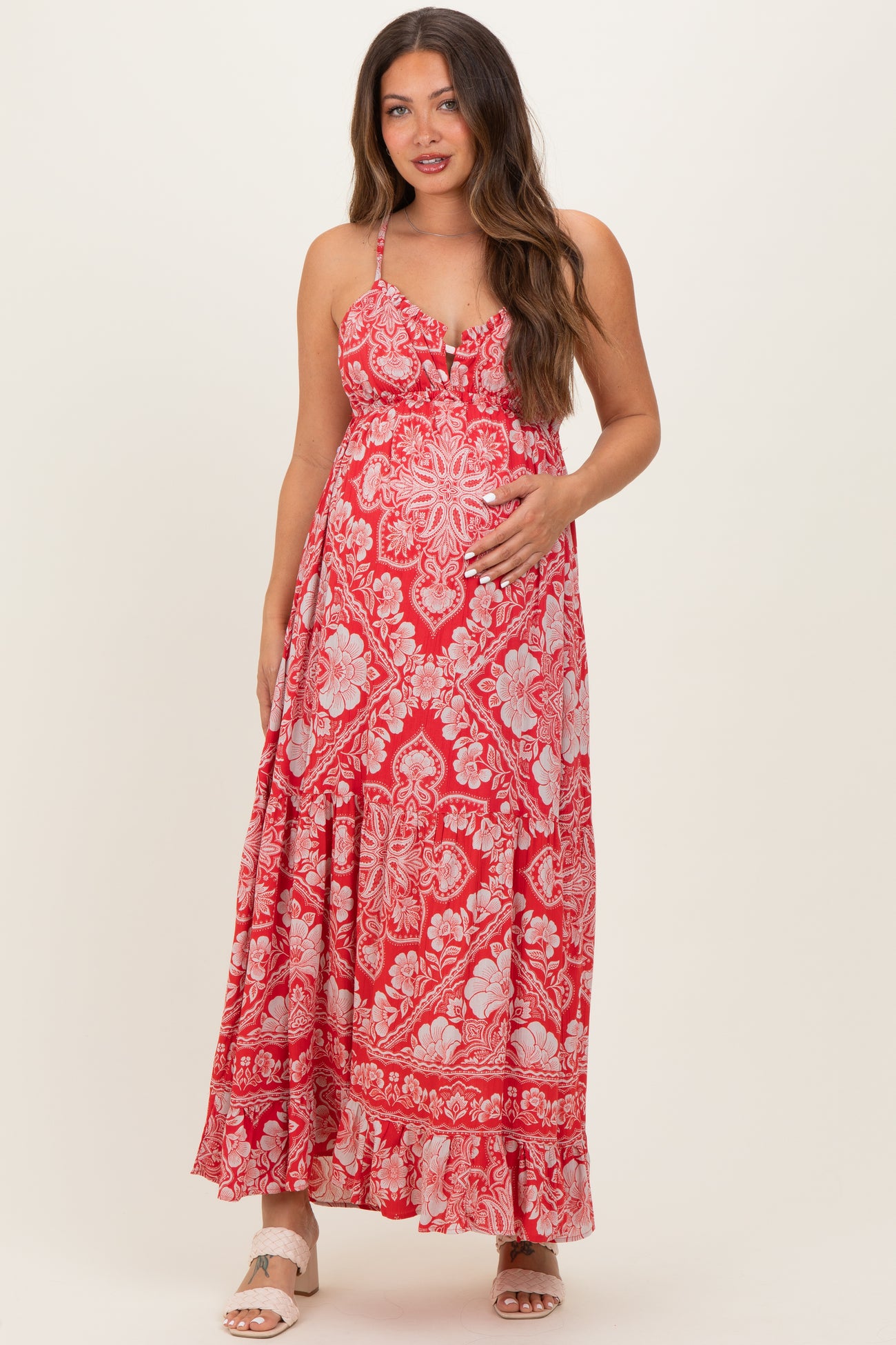 woman wearing a red floral maternity maxi dress with spaghetti straps and holding her baby bump