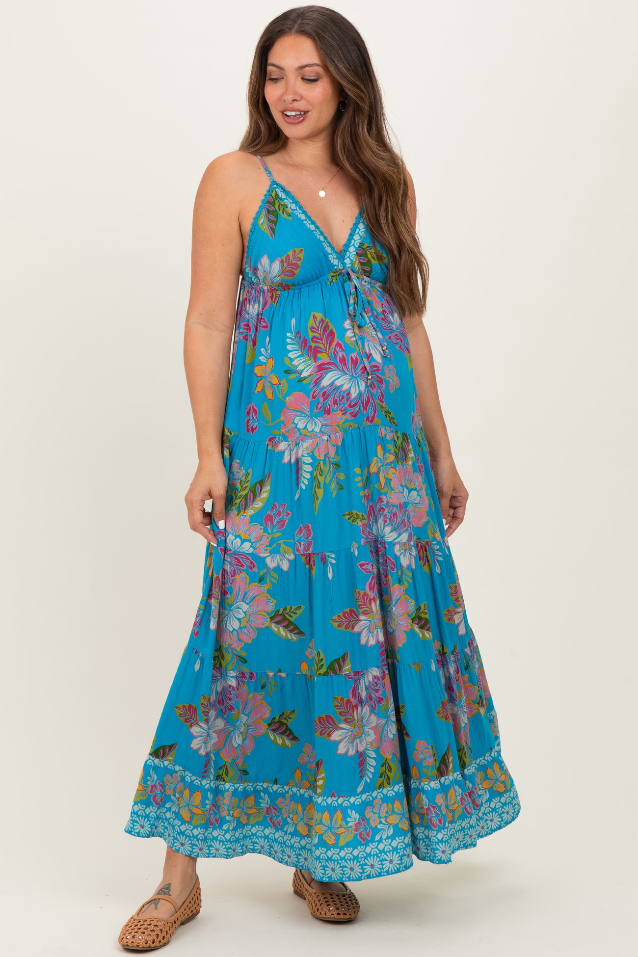 woman wearing a turquoise floral maxi dress with adjustable straps and a tiered skirt, showcasing her baby bump