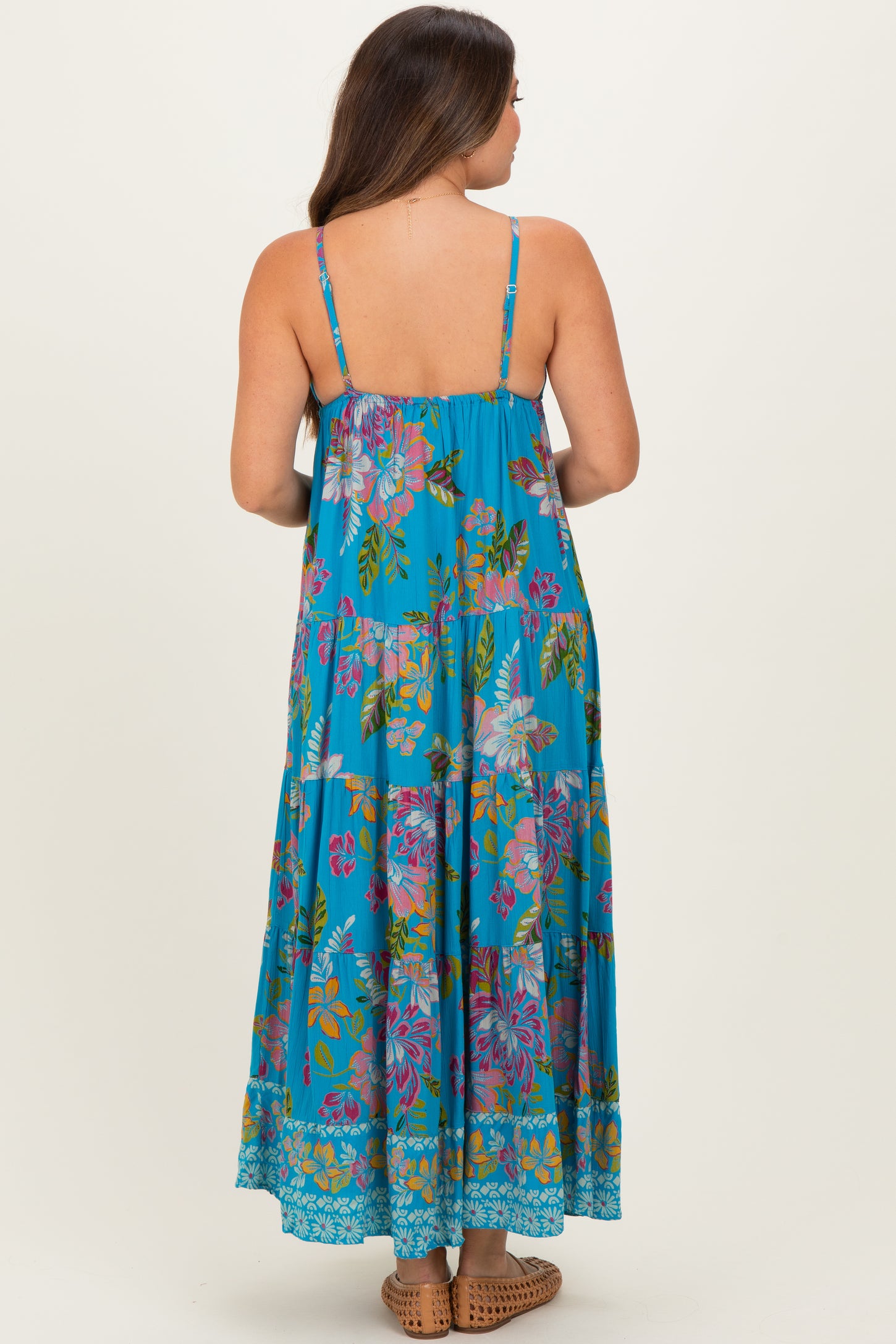 woman wearing a blue floral print maternity maxi dress with spaghetti straps and tiered design, showing her pregnant belly