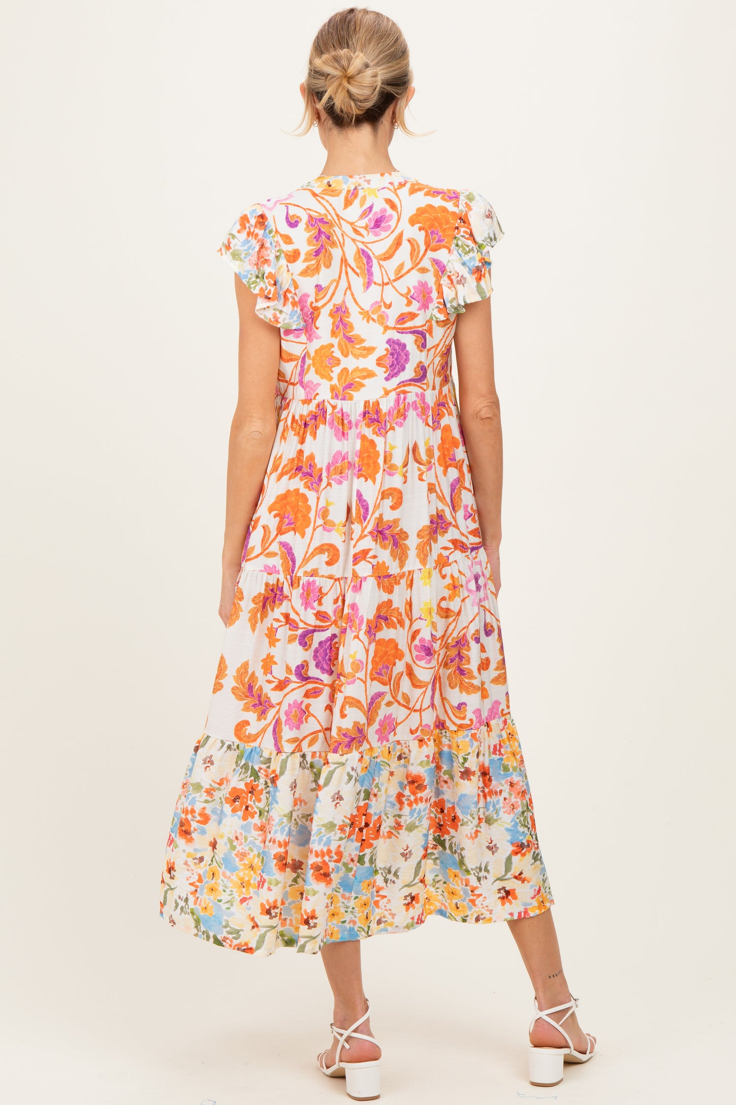 woman wearing a floral print maternity maxi dress with ruffled sleeves and a flowing skirt, showing a baby bump