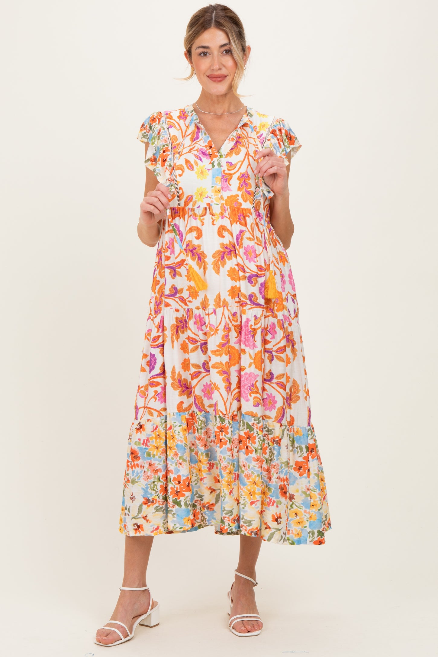 woman wearing a floral maternity dress with ruffled sleeves and a tiered skirt, holding her baby bump