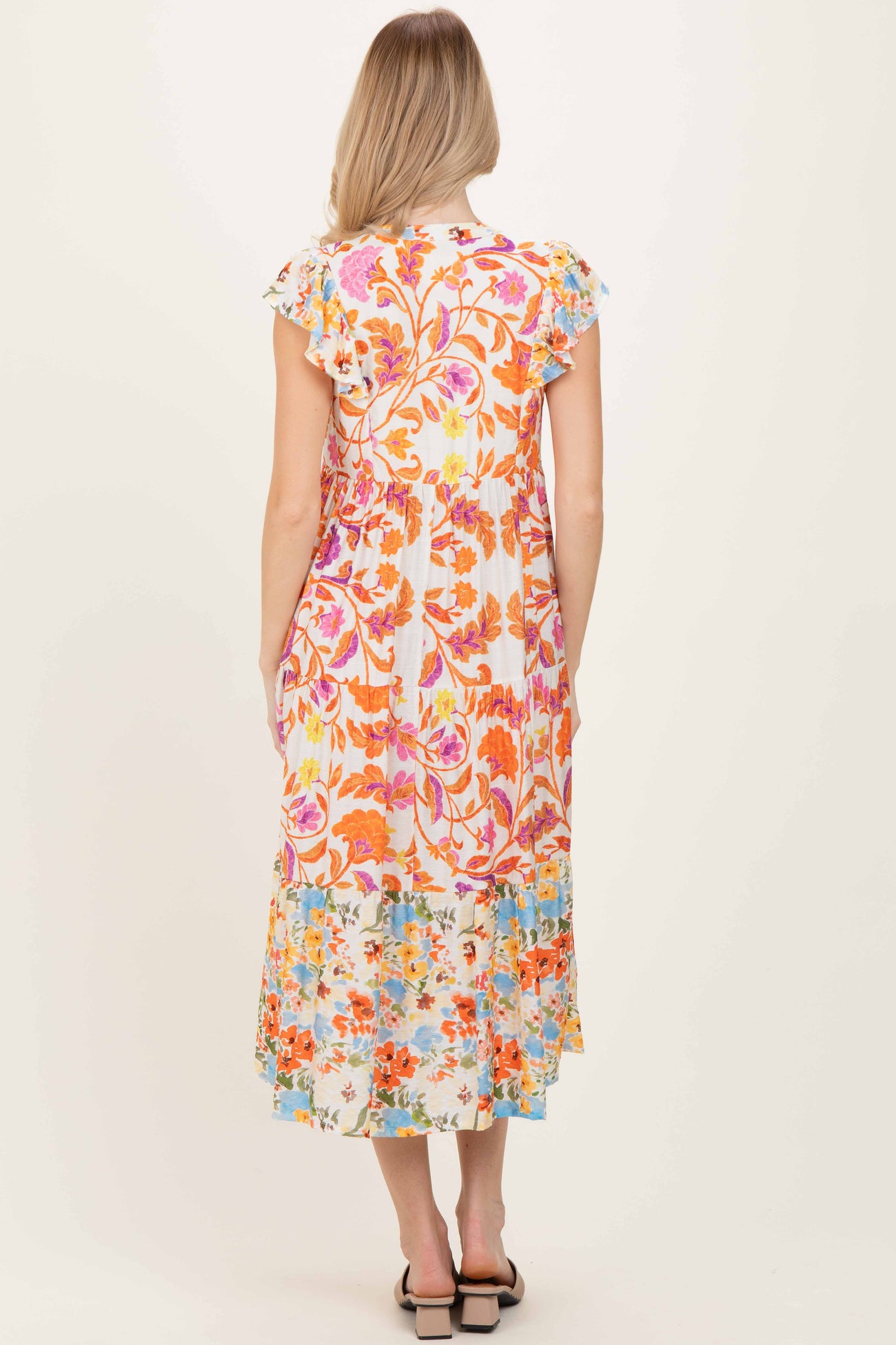 woman wearing a colorful floral print maxi dress with ruffled sleeves and a tiered hem, viewed from the back