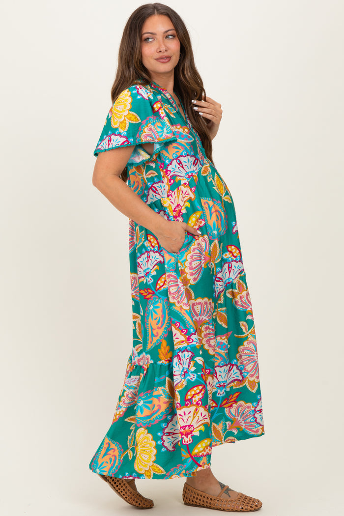 woman wearing a vibrant floral print maxi maternity dress with short sleeves and pockets, showcasing her baby bump