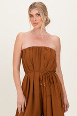 woman wearing a strapless rust-colored jumpsuit with a gathered elastic top and a tied waist belt