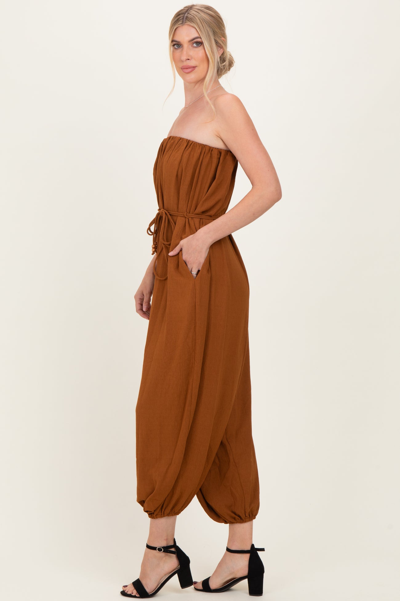 woman wearing a rust colored strapless jumpsuit with a drawstring waist and harem-style pants