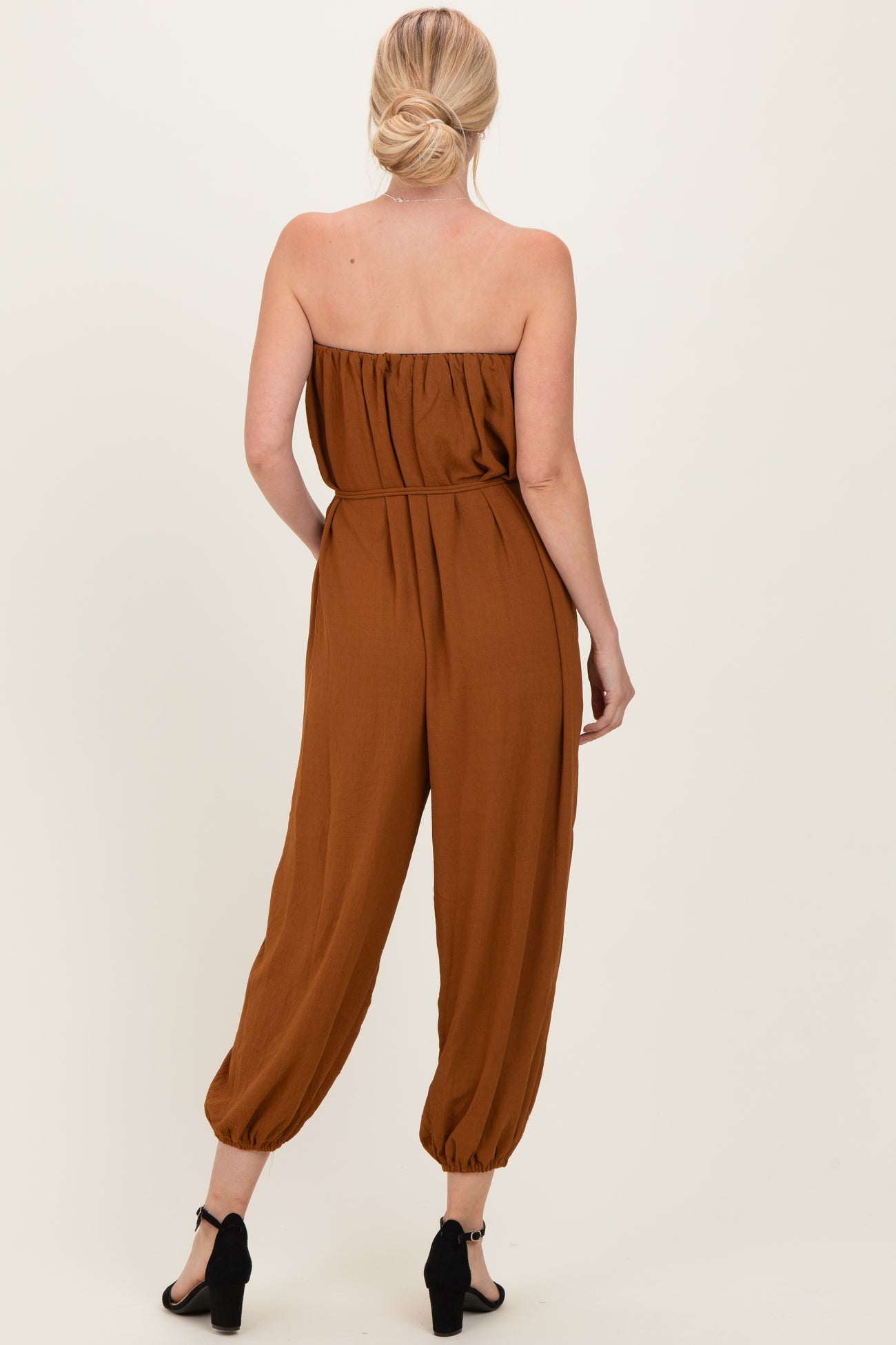 woman wearing a brown strapless jumpsuit with a loose fit and tapered ankles, shown from the back