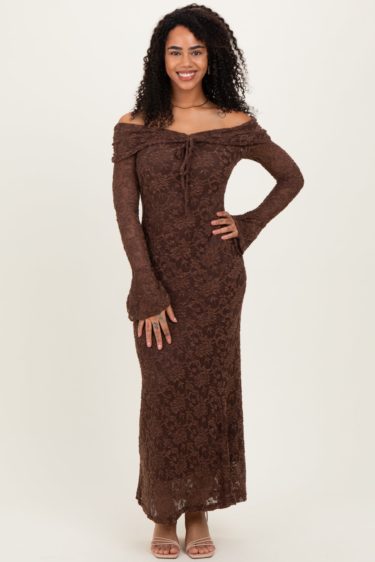 woman wearing a brown off-the-shoulder lace maxi dress with long sleeves and a tie detail at the neckline