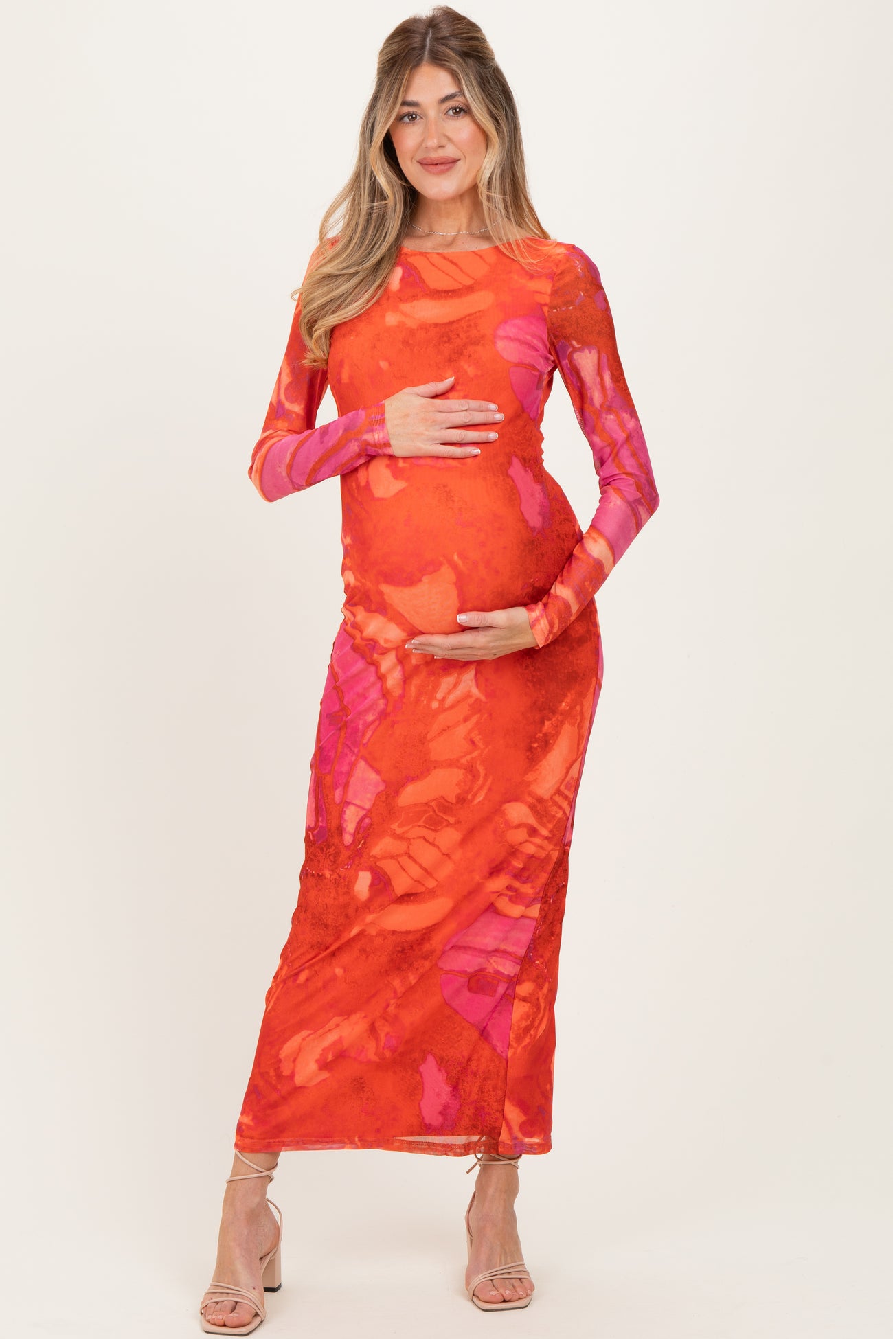 woman wearing a red and pink floral print maternity dress and holding her baby bump