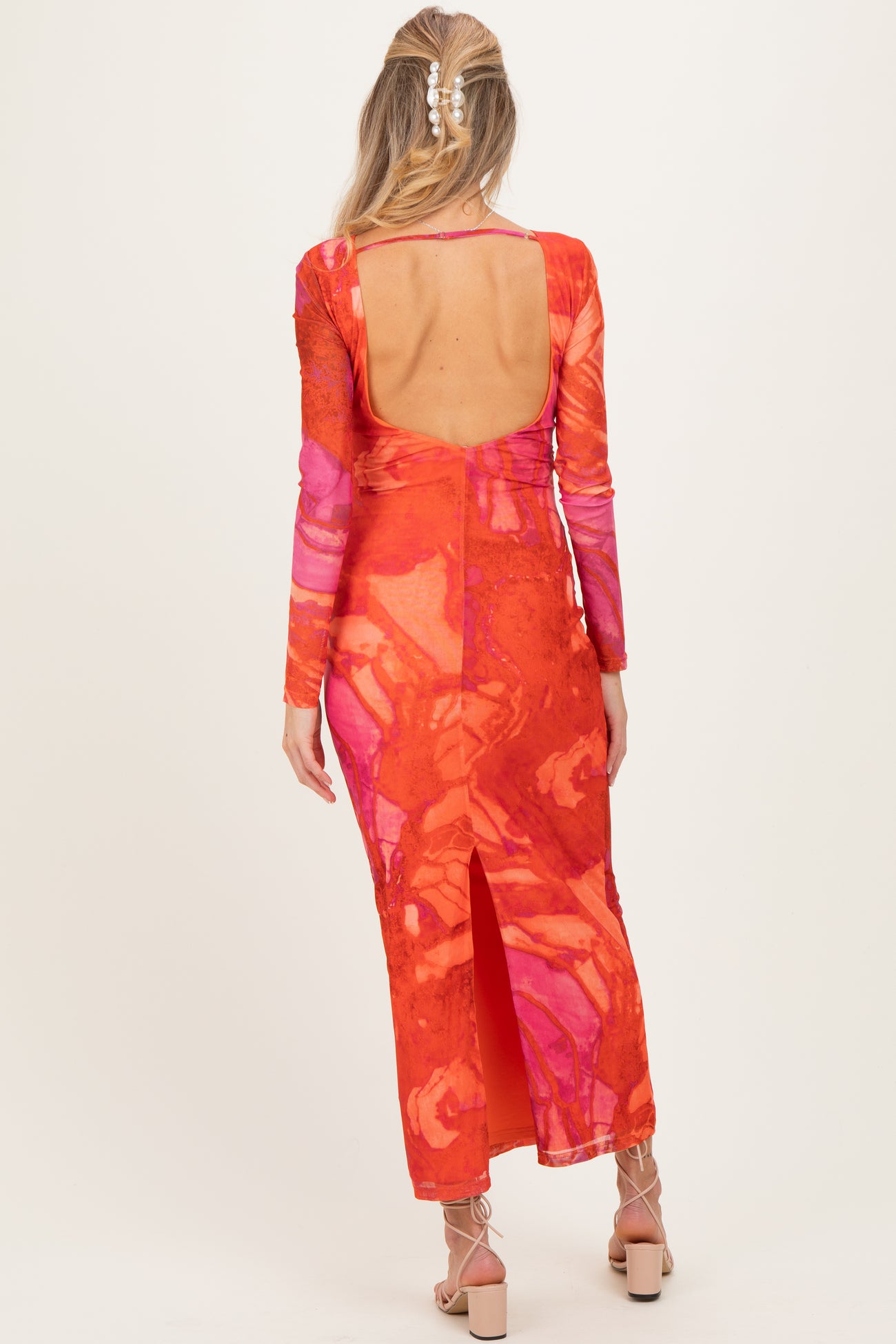 woman wearing a vibrant orange and pink long sleeve maternity dress with a low back and side slit