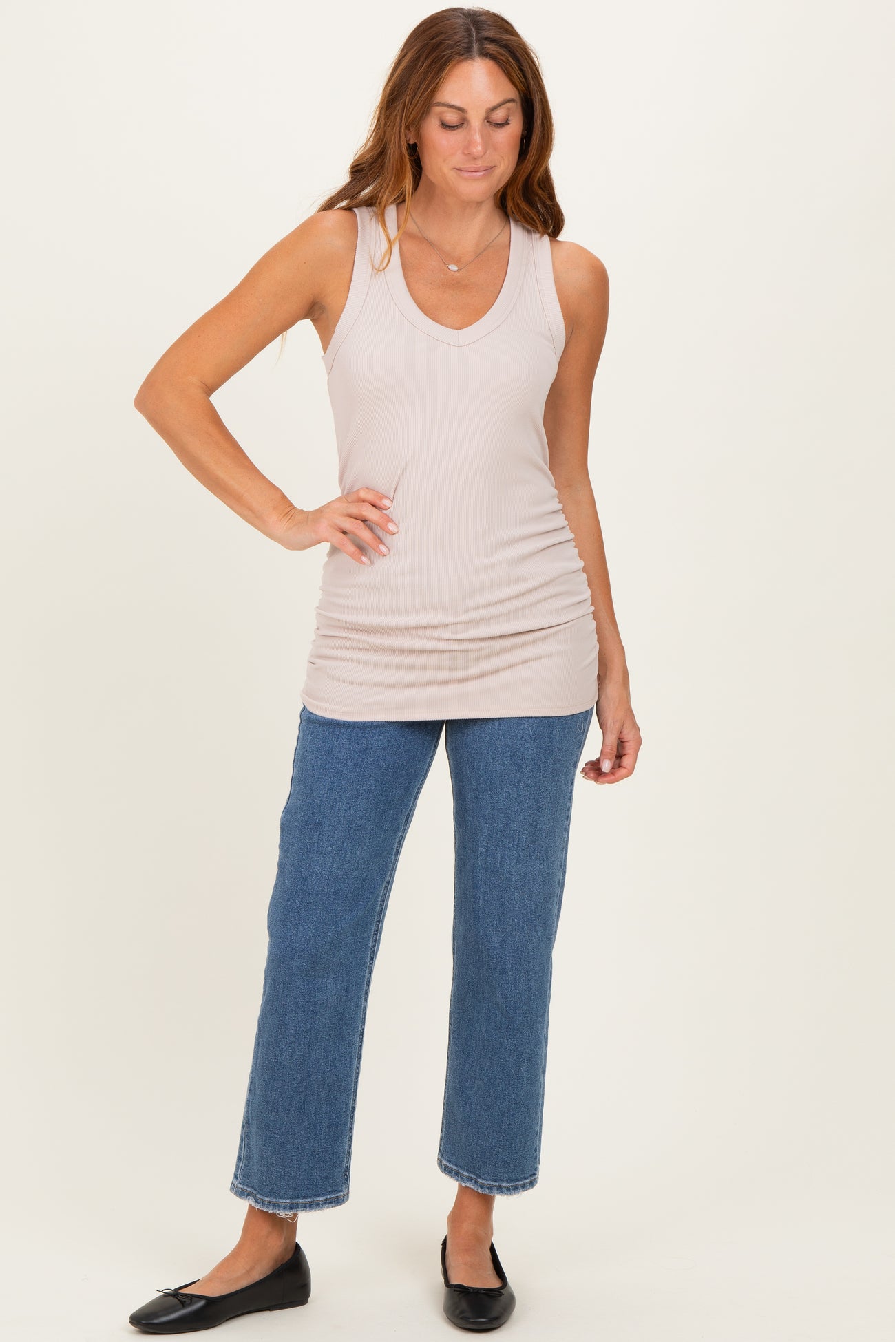 woman wearing a beige ribbed tank top and high-waisted cropped jeans, styled with black flats