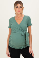 woman wearing a green maternity top with a v-neck and tie detail, accentuating her baby bump