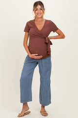 woman wearing a rust brown wrap maternity top with a tie detail and blue wide-leg maternity jeans, showing her baby bump