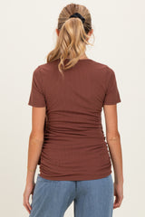 woman wearing a rust-colored short sleeve maternity top with a fitted silhouette and gathered detailing at the sides