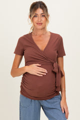 woman wearing a brown maternity wrap top with a tie detail and holding her baby bump
