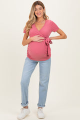 woman wearing a pink short sleeve maternity wrap top and holding her baby bump, paired with light blue jeans