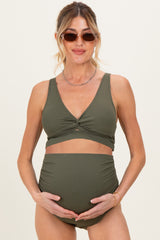 woman wearing an olive green maternity bikini with a V-neck top and high-waisted bottoms, holding her baby bump