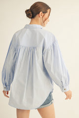 woman wearing a light blue oversized button-up shirt with puffy sleeves and a gathered back detail