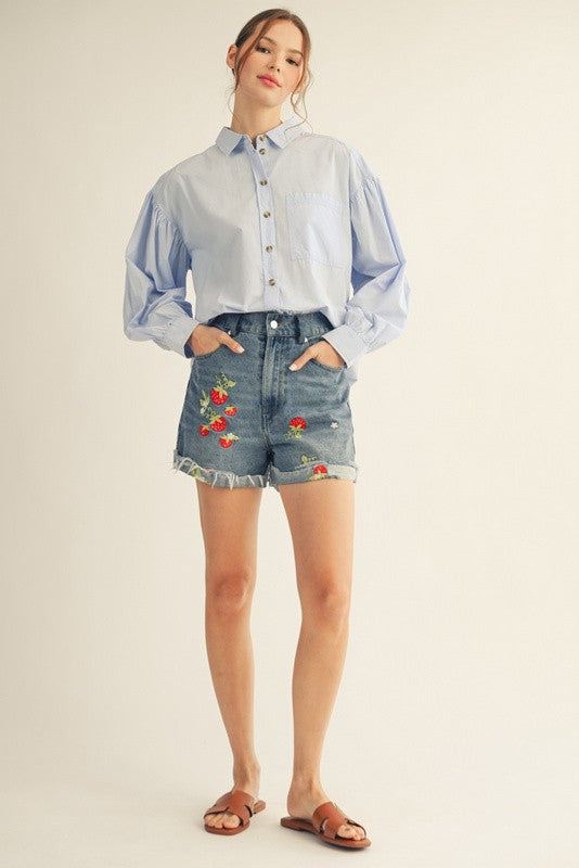 woman wearing a light blue button-up shirt with puff sleeves and high-waisted denim shorts with floral embroidery