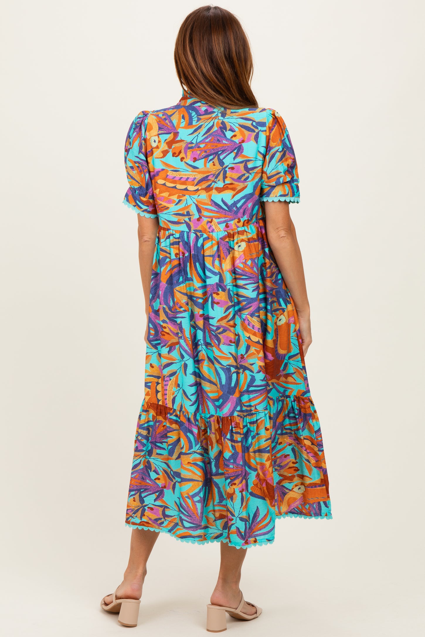 woman wearing a colorful tropical maxi dress with short sleeves and ruffle hem, seen from the back