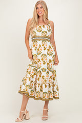 woman wearing a white floral maxi dress with a tiered skirt and spaghetti straps, paired with nude heeled sandals
