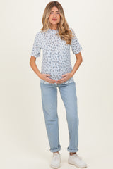 woman wearing a light blue floral maternity top and light wash jeans, cradling her baby bump