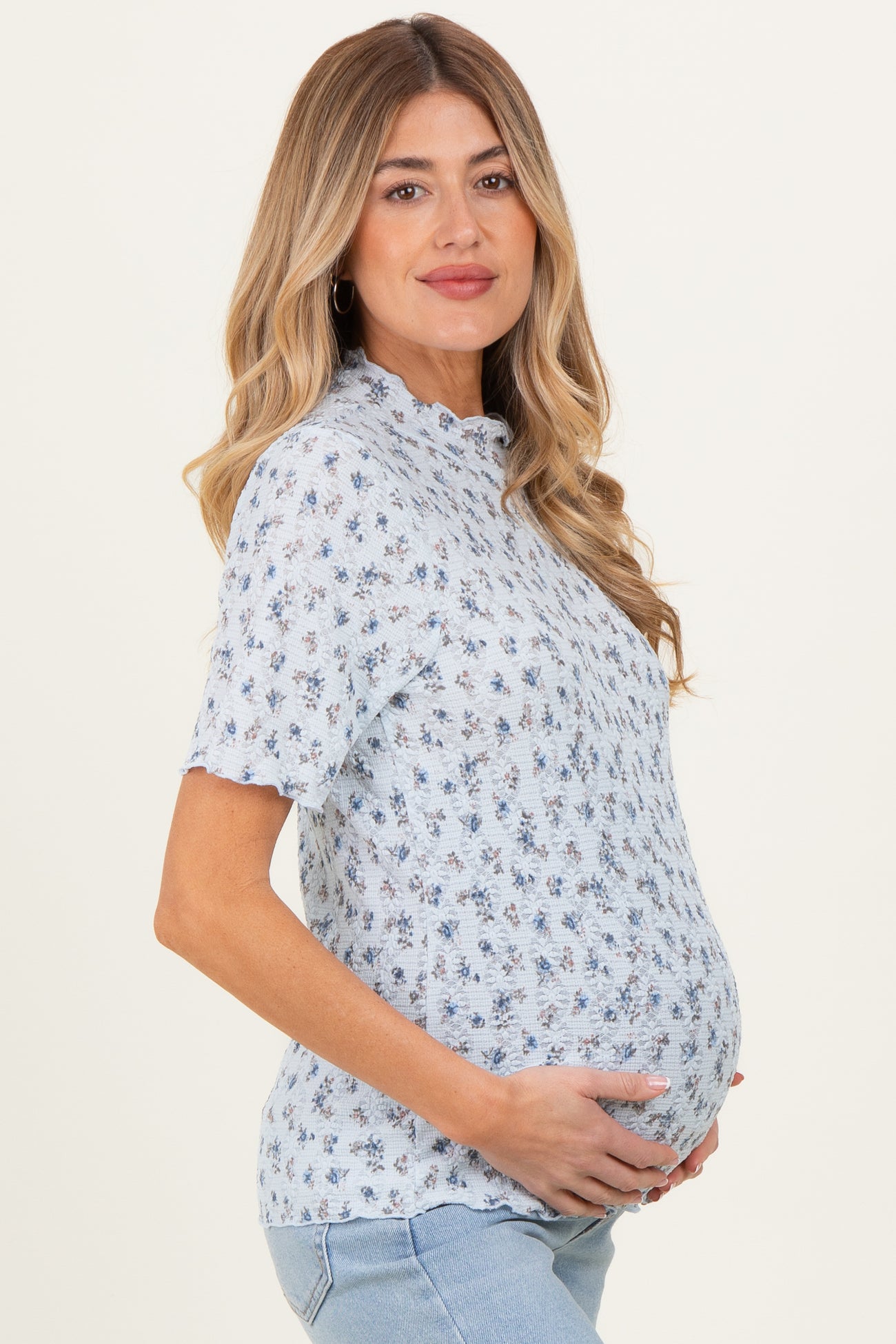 woman wearing a light blue floral maternity top and holding her baby bump