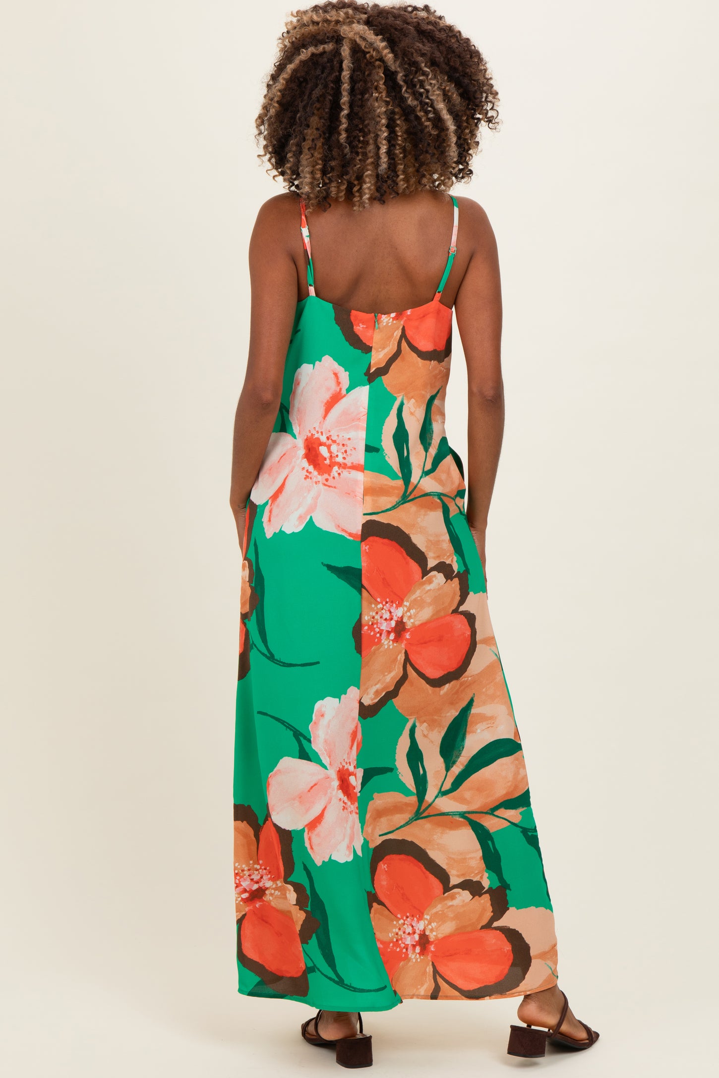 woman wearing a floral green and orange maternity maxi dress with spaghetti straps, showing her back and long hair