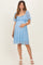 woman wearing a light blue lace maternity dress with flutter sleeves and holding her baby bump