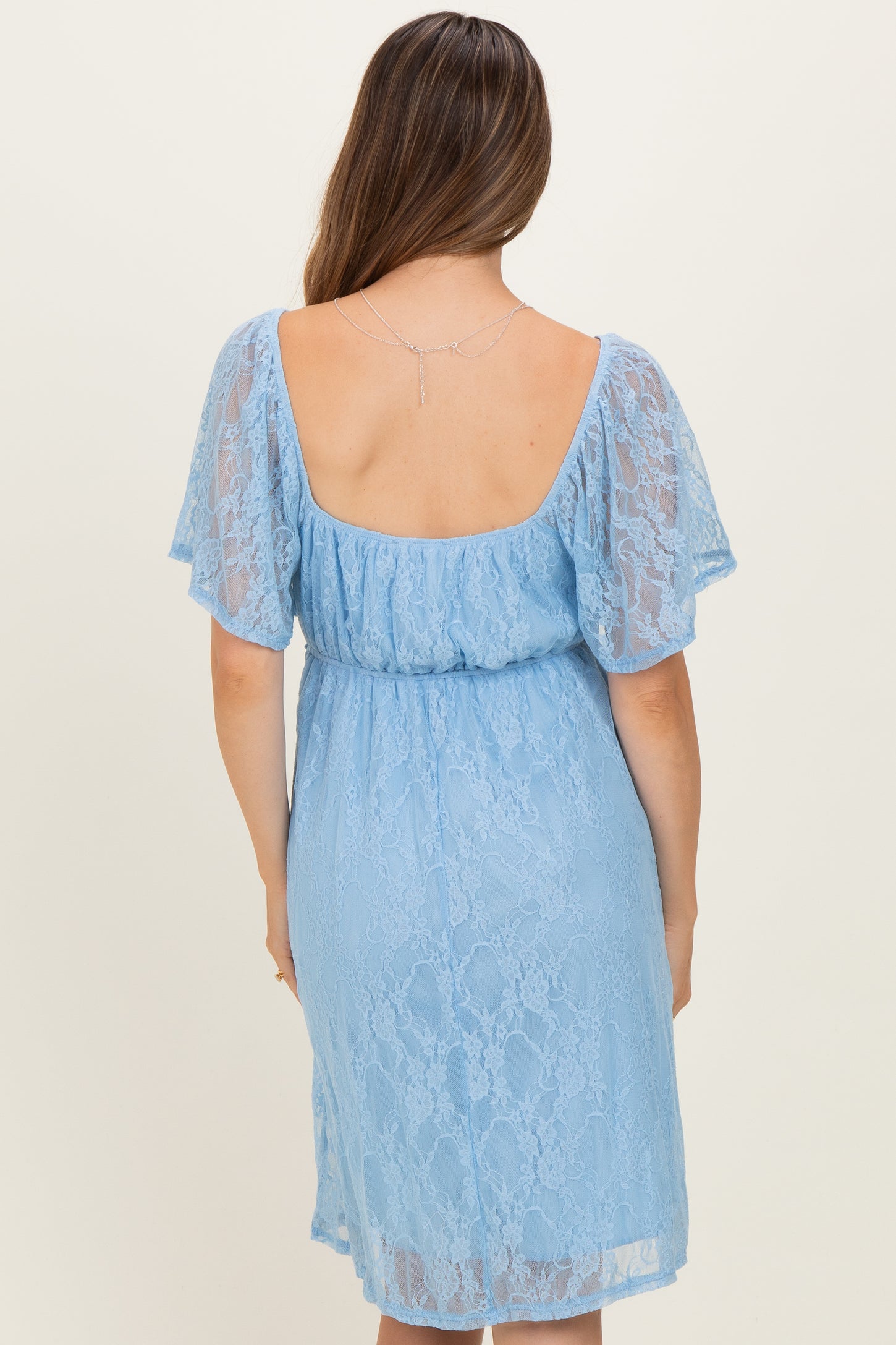woman wearing a light blue lace maternity dress with flutter sleeves and a cinched waist seen from the back